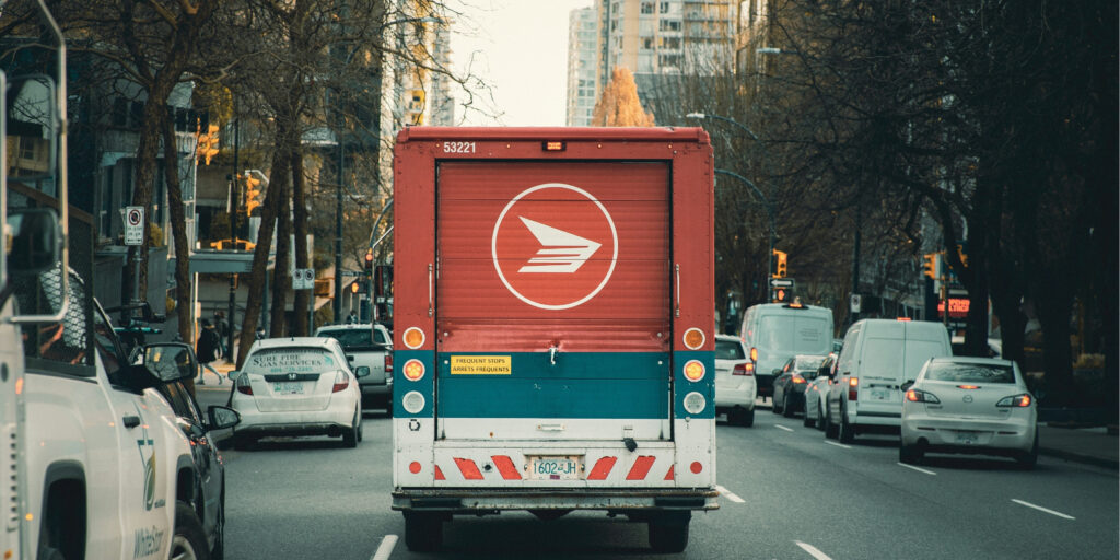 An image of a Canada Post truck driving down a city street, used as a header for a blog listing Canada Post alternative carriers in the event of a Canada Post strike