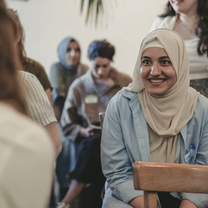 A young women with a hijab smiling in a conversation with another person